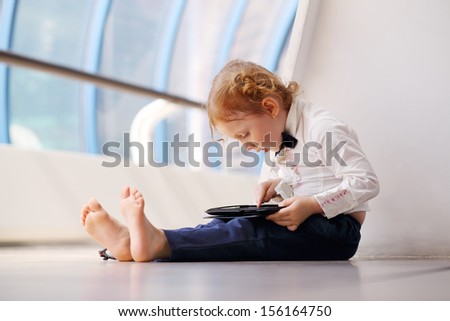 Little cute barefoot girl sits on floor and plays with tablet pc in gallery.