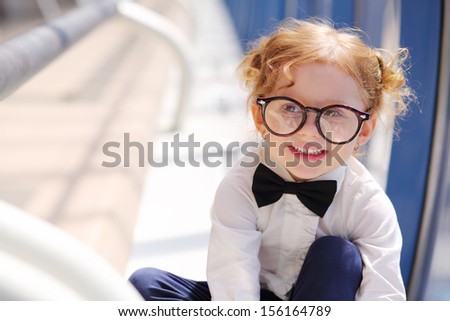 Little cute red hair girl in glasses sits on floor in gallery near window.