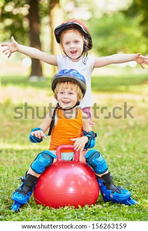 Little boy sits on red ball for jumping, girl stands behind him with her arms outstretched to sides