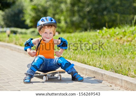 Little skateboarder sits on park alley on skateboard with arms akimbo