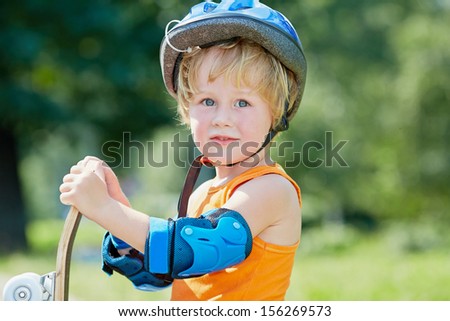 Half-length portrait of little boy who stands half-turned with skateboard in park