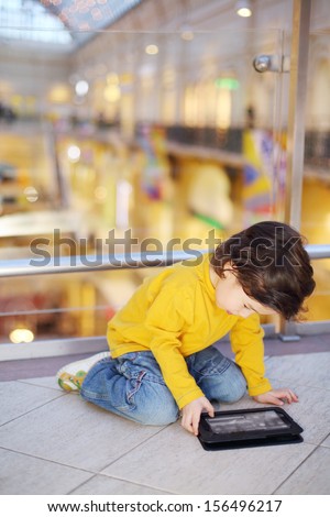 Little cute boy in jeans plays with tablet pc on floor in mall.