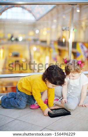 Little cute girl and boy play with tablet pc on floor in mall.