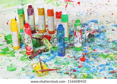 Bottle of paint and brushes on the floor with multicolored stains of paint