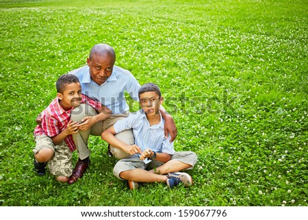 Portrait of squatted african father with two little sons on green lawn