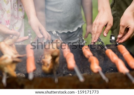 Three people turn around skewers on the grill