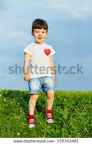 Little boy in shorts and white t-shirt with pinned red heart goes down grassy slope
