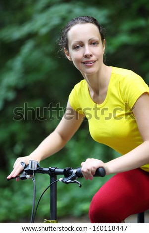 Beautiful happy woman in yellow rides bicycle in park at summer day.