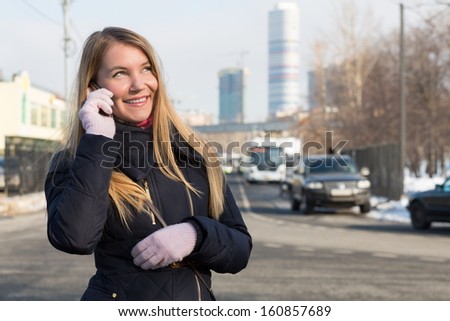 The girl in warm clothes talking on the phone on the street on the background of skyscrapers