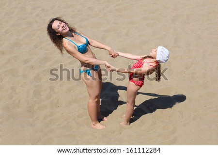 A young woman with a little girl standing on the sand hand-in-hand
