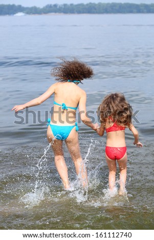 Back view of young mother and daughter jumping in water holding hand