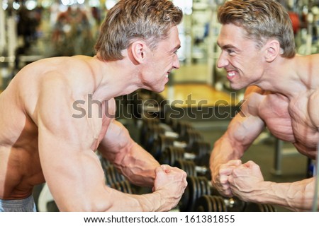 Grinning bodybuilder poses in gym hall demonstrating muscles in front of mirror