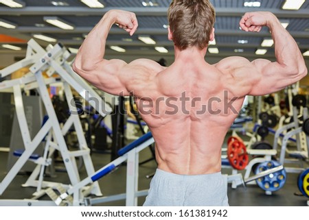 Bodybuilder poses in gym hall demonstrating tense muscles of his back