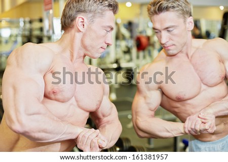 Bodybuilder poses in gym hall demonstrating muscles in front of mirror