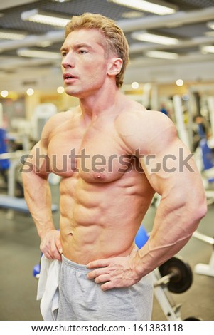Man gets some rest between exercises standing with his hands akimbo in gym hall