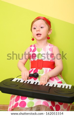Little girl in a bright lush dress playing on a toy piano and sings