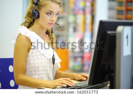 A beautiful student sitting at a computer wearing headphones in the library hall