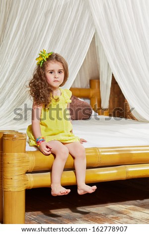 Little girl sits on edge of bed with bamboo frame