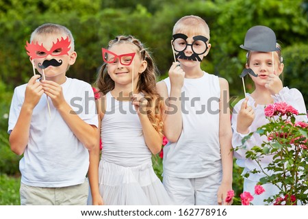 Children stand together in summer park holding masks on stiks at their faces