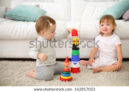 Two pretty kids sit on carpet and play with toys near sofa. Focus on left kid. Shallow depth of field.