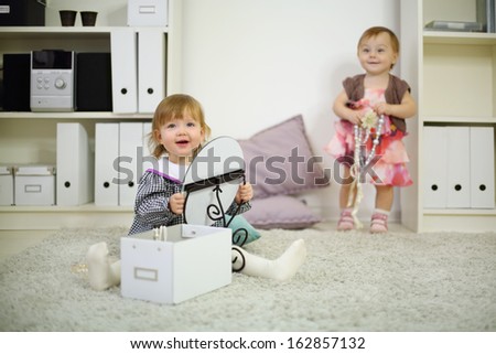 Two happy little girls play on white carpet with mirror and beads at home. Shallow depth of field. Focus on left kid.