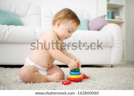 Cute little kid in diaper sits on carpet and plays with pyramid at home. Shallow depth of field.