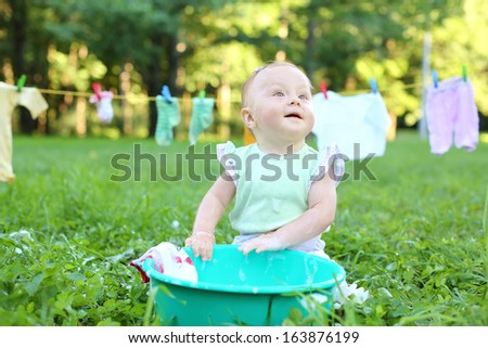 The little girl washes clothes in a small green basin near the rope with drying clothes