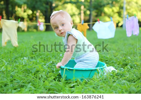 Funny little girl in a small basin with foam near the rope with wash clothes