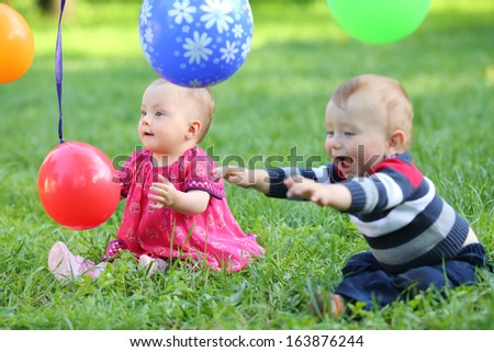 Little girl and boy is playing with colorful balloons, which is tied to a rope in the park