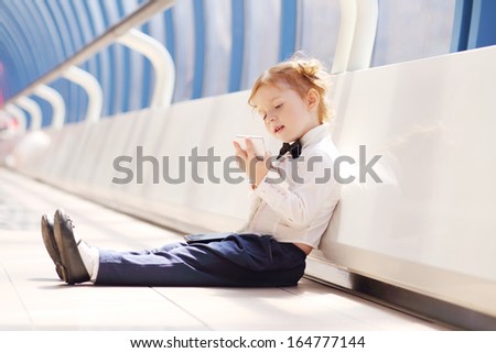 Little cute girl sits on floor and holds white cell phone in long gallery.
