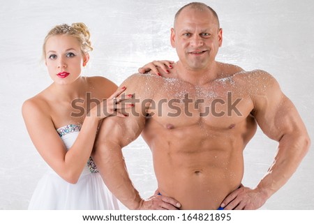 A strong man with snow on body and beautiful girl in white dress in studio