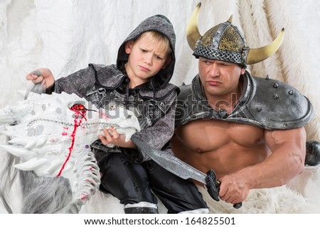 A muscular man with young son in costume viking with a sword and dragon head
