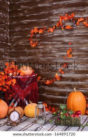 Pumpkins, old lamp, clock and basket of fruits on rug in room with wooden walls and autumn interior.