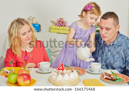 Little birthday girl pours out tea to her parents sitting at birthday table