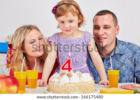 Happy family of three sits at birthday table and looks at burning candle on cake