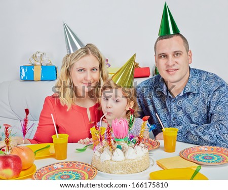 Mother, father and little daughter sit together at birthday table