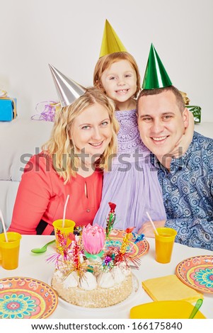 Smiling little girl hugs her parents when they sit together at birthday table