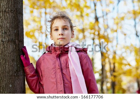 Half-length portrait of little girl standing at tree in autumn park