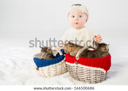 Surprised baby girl dressed in white fur with two basket with small kittens
