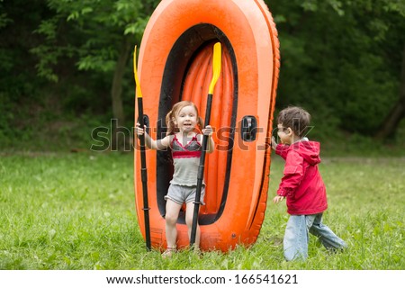 Two children play with paddles and big rubber boat on the nature