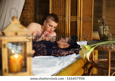 Beautiful woman and young man lie on bamboo bed and look at each other in bedroom.