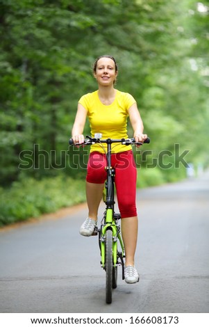 Smiling woman in sport clothes rides bicycle in park at summer day.