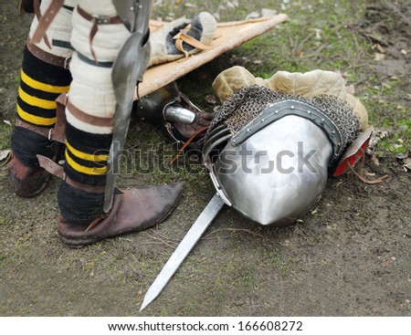 Legs of man and armored metal medieval helmet on ground outdoor.