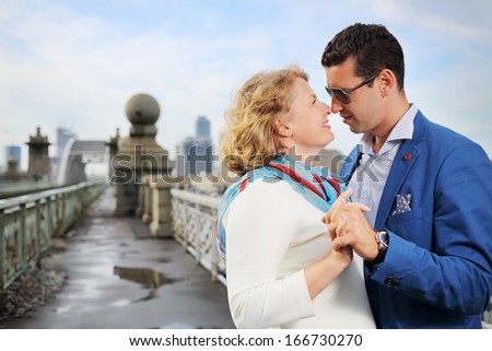 Pregnant woman in white and stylish man touch each other noses on street.