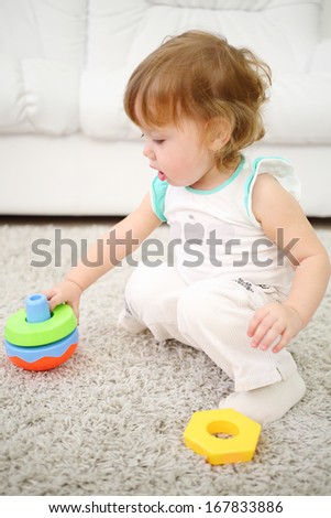 Cute little girl sits on carpet and plays with toy at home. Shallow depth of field.