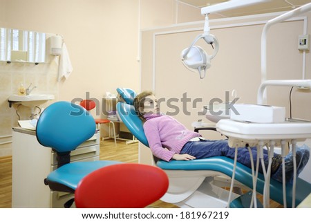 Pretty girl lies on dental chair in office, looks up and waits for doctor