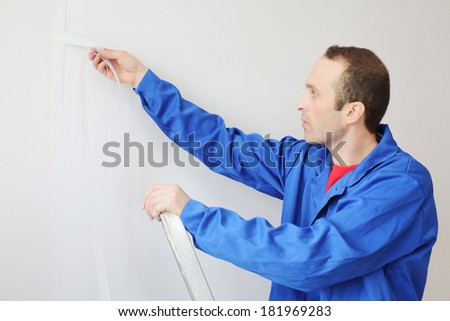 Worker in blue clothes works with painting fiberglass in new apartment