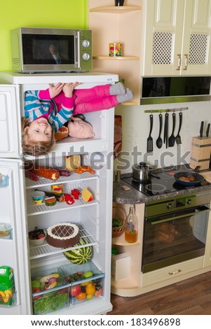 Little girl sits in freezer refrigerator in the kitchen at inverted house