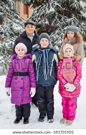 Family of five stands outside in winter under snow-covered firtrees