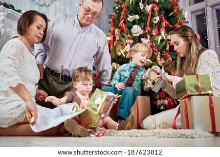 Mother, father and three children examine content of gift boxes under Christmas tree, low angle view
